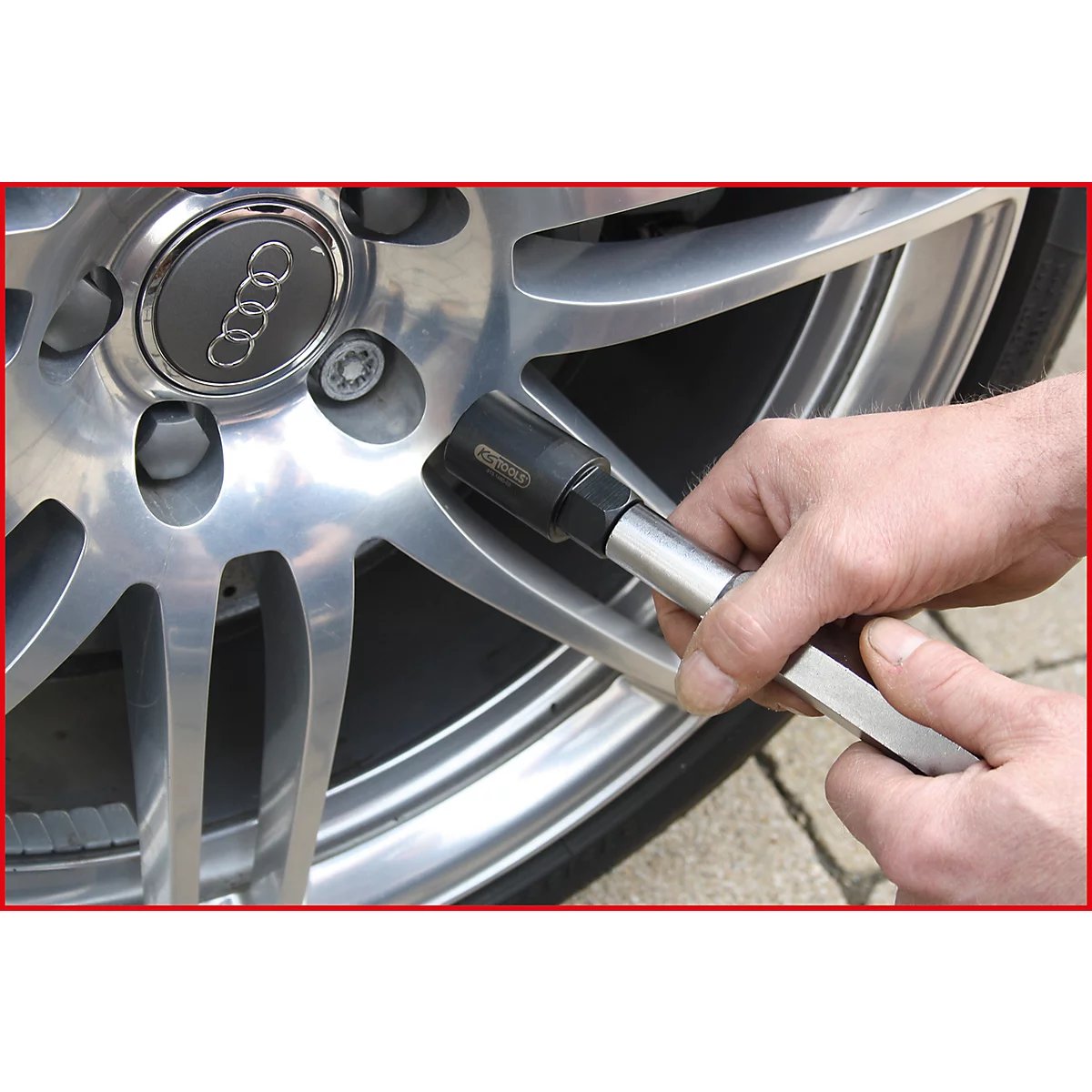 Hand mit Werkzeug an einem Alufelgen-Rad. Im Hintergrund ist ein Audi-Logo zu sehen.